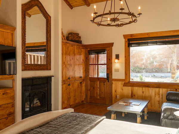 A cozy room with wooden interior features a bed, fireplace, TV, chandelier, and a window letting in natural light.