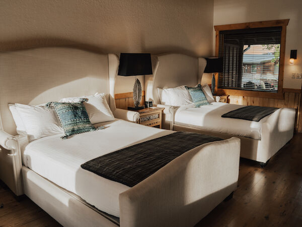 The image shows a cozy bedroom with two large beds, elegant bedding, side tables, and soft lighting from lamps, creating a serene ambiance.