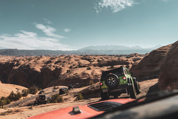 Off-road vehicles navigating a rocky desert landscape under a clear sky, with mountains in the distance.