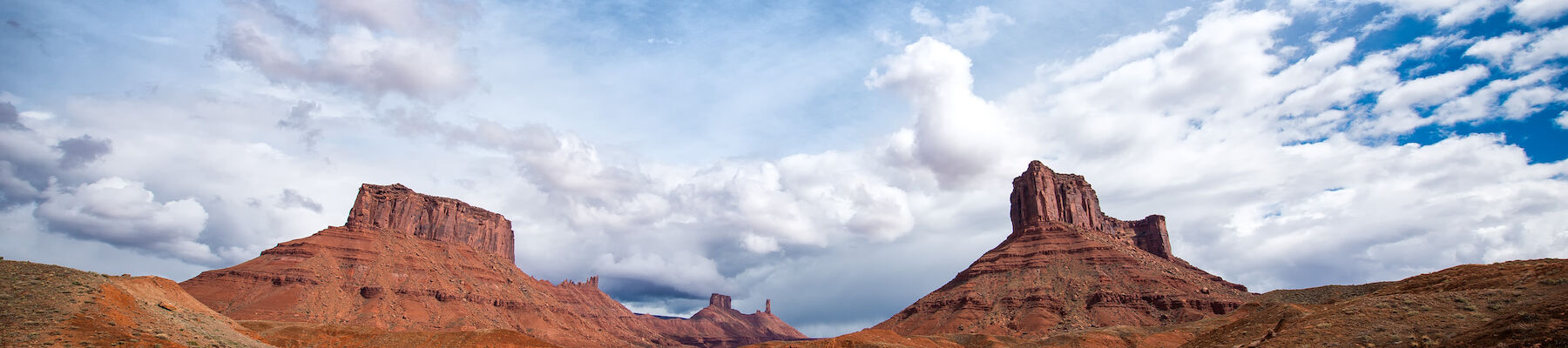 The image shows a desert landscape with red rock formations and buttes under a partly cloudy sky. The terrain is mostly barren with sparse vegetation.