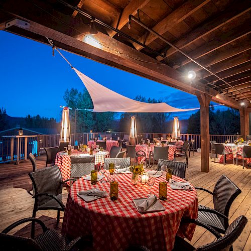 The image shows an outdoor restaurant dining area with wooden flooring and tables covered in red checkered cloths under a clear evening sky.