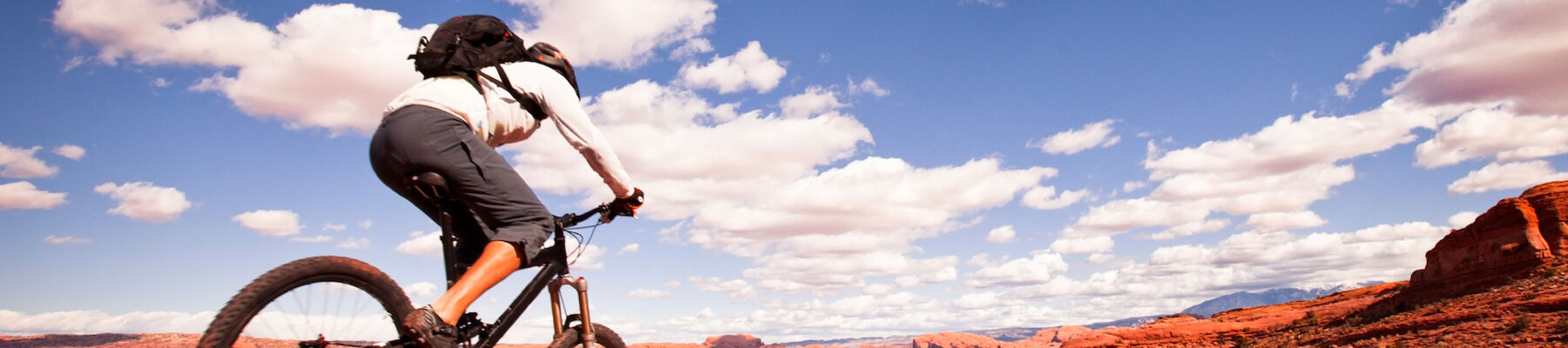 A person riding a mountain bike on a rocky, red terrain under a bright blue sky with scattered clouds, enjoying an outdoor adventure.