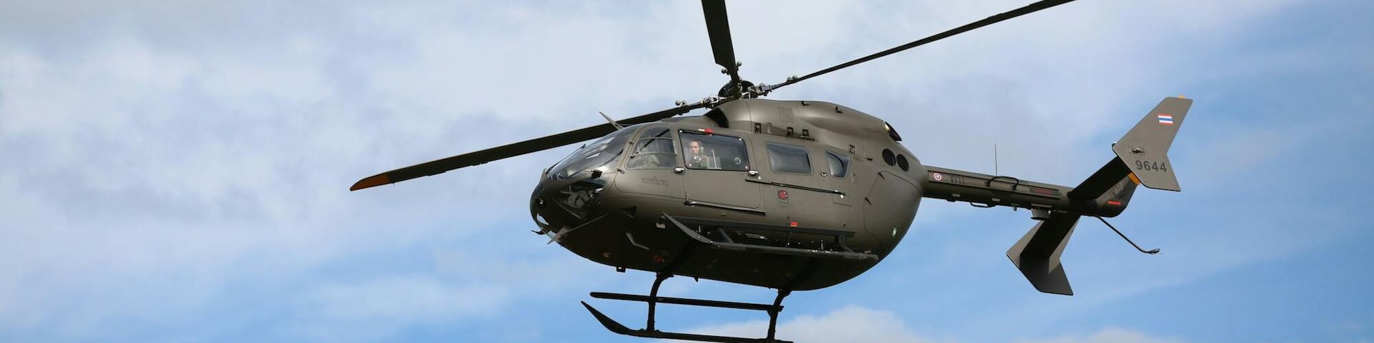 A helicopter is flying in the sky with a background of scattered clouds and blue sky.