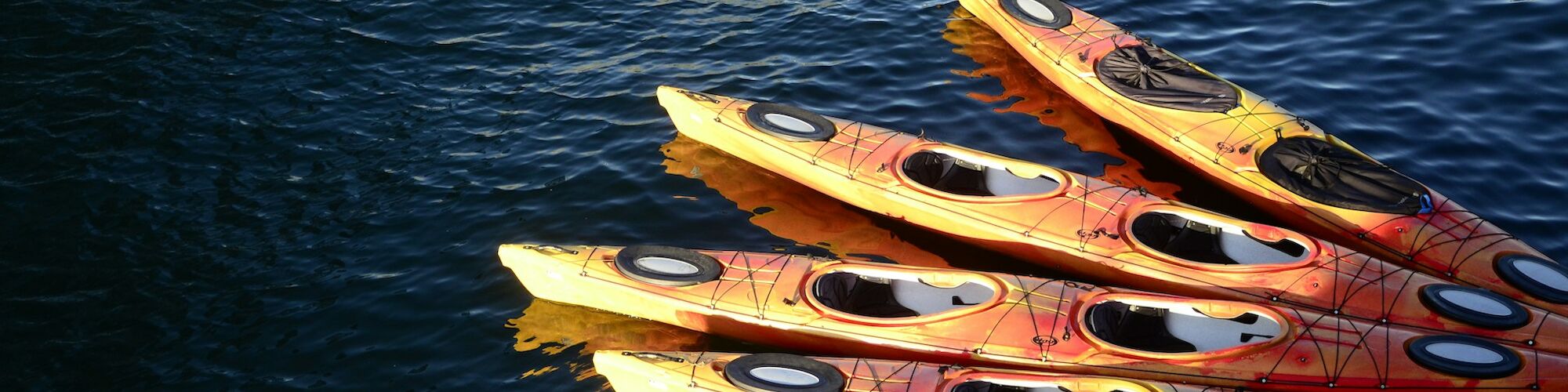 A group of orange and yellow kayaks are lined up on the water, with one blue kayak apart from them.