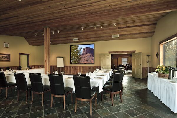 The image shows a conference room with a U-shaped table arrangement, chairs, a large screen displaying a landscape, and a refreshment table to the side.