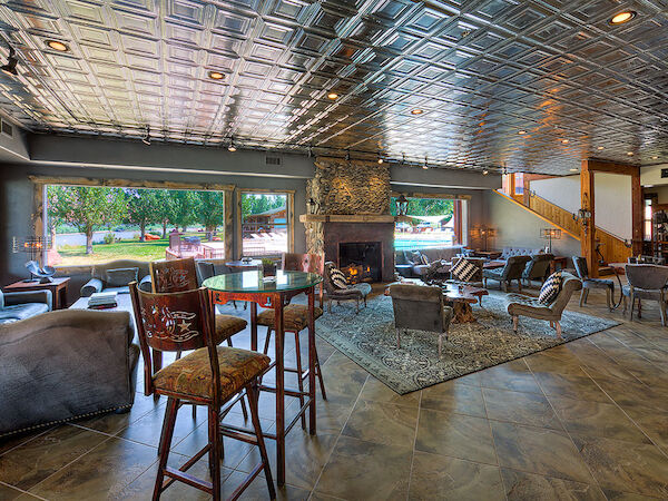 A spacious lounge area with a tiled ceiling, comfortable seating, a fireplace, and large windows overlooking a green outdoor area.