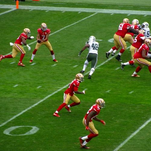 The image shows a football game in progress, with players in red uniforms likely setting up for a play while players in white defend.