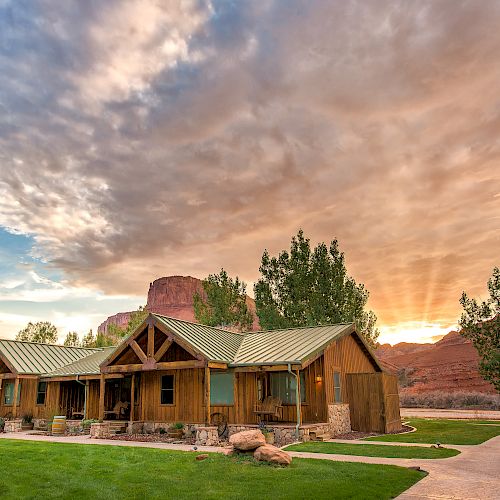 The image shows a charming wooden house with a green roof, surrounded by trees. It's set against a stunning sunset, creating a serene atmosphere.