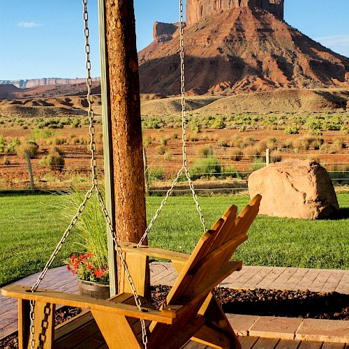 A wooden porch swing hangs under a covered patio, overlooking a scenic, rocky desert landscape with a prominent butte in the distance.
