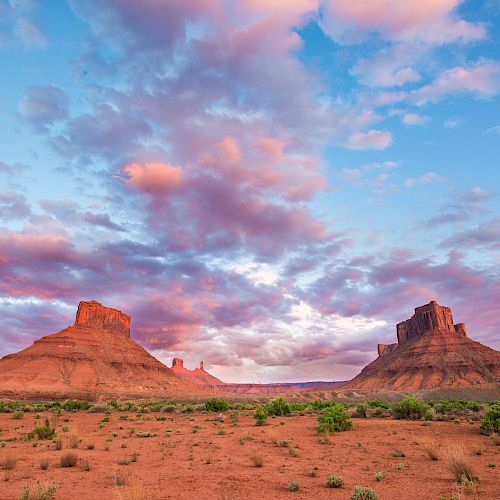 The image shows a desert landscape with two large, flat-topped rock formations under a sky filled with clouds during sunset or sunrise.