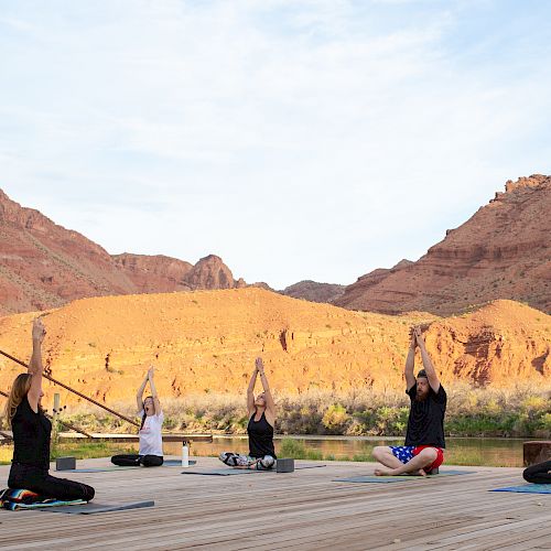 A group of people practicing yoga outdoors on mats, set against a backdrop of red rocky hills and a clear sky, ending the sentence.