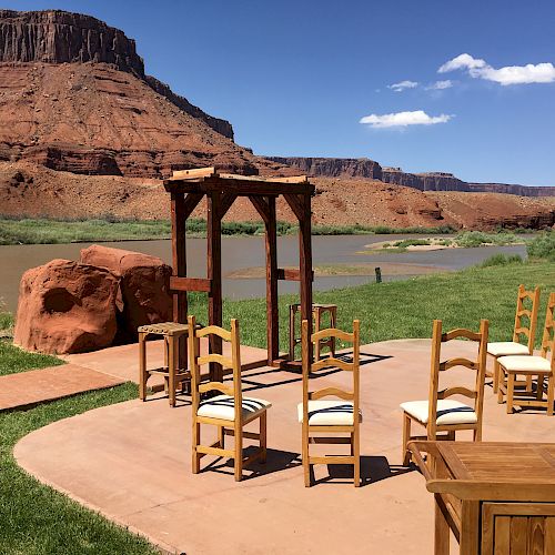 Outdoor setup with chairs and an arch, overlooking a river and red rock formations under a clear sky with scattered clouds, suggesting an event.