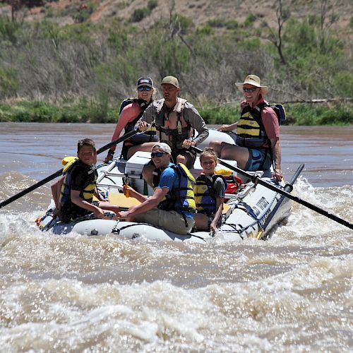 A group of people wearing life jackets are whitewater rafting on a river, navigating through rough waters in an inflatable raft, looking focused.