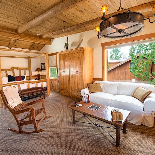 A cozy rustic room with a canopy bed, rocking chair, white sofa, wooden furniture, large windows, and decorative lighting.