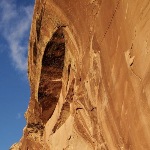 A natural rock formation with an arch in a desert landscape, with clear blue sky in the background, against the rocky cliff face.