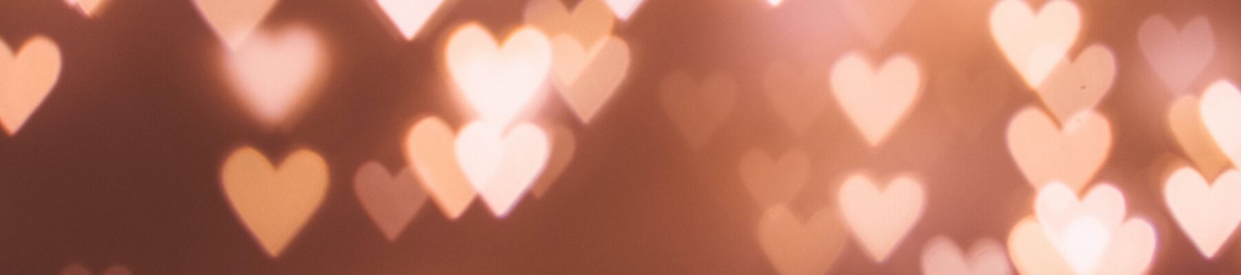 The image shows a blurred background with multiple glowing heart shapes of light, creating a warm and romantic atmosphere.