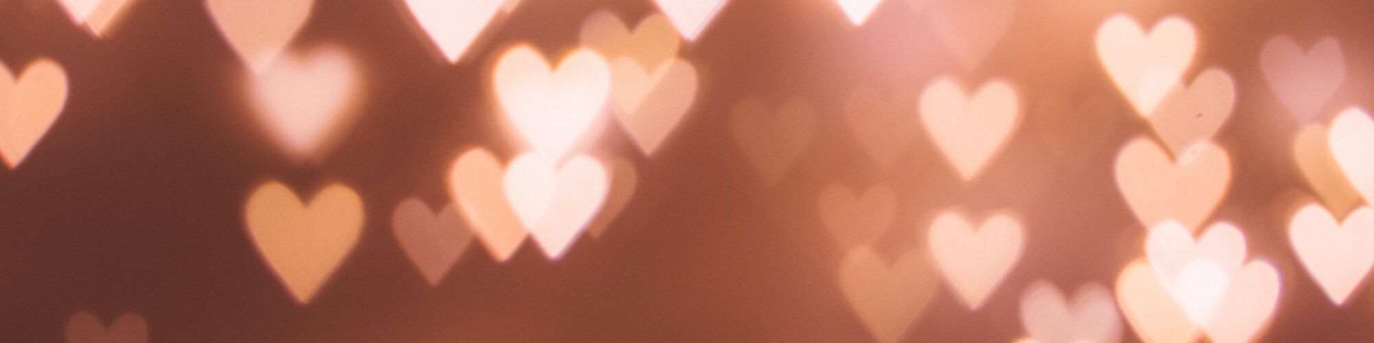 The image shows a blurred background with multiple glowing heart shapes of light, creating a warm and romantic atmosphere.