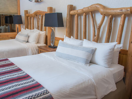 A cozy bedroom with two beds featuring rustic wooden headboards, striped blankets, white linens, and two bedside tables with black lamps.