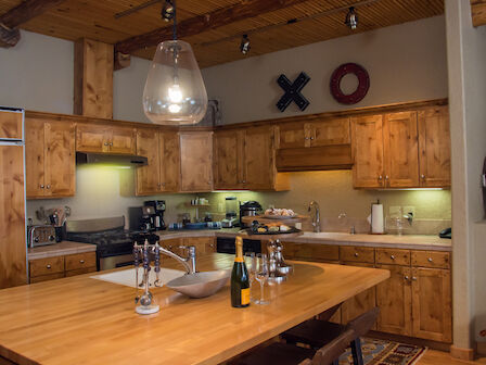 A rustic kitchen with wooden cabinetry, stainless steel appliances, a large island with a light fixture, and various kitchen items and decor.