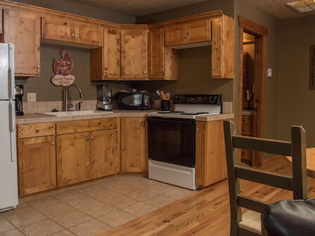 A kitchen with wooden cabinets, a white fridge, stove, microwave, and other appliances, alongside a small dining table and chairs.