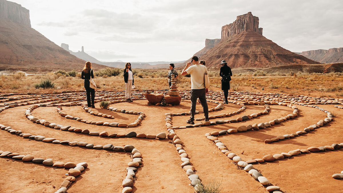 People exploring a labyrinth made of stones in a desert landscape with mesas in the background.