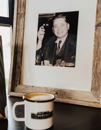 A framed black-and-white photo of a man with a cigar is beside a white mug on a table.