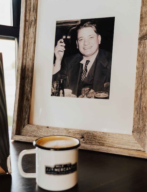 A framed black-and-white photo of a man with a cigar is beside a white mug on a table.