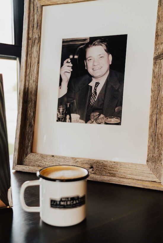 A framed black-and-white photo of a man with a cigar is beside a white mug on a table.