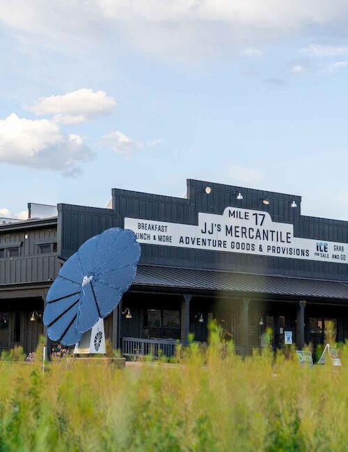 A rustic building labeled "Jim Mercantile" with surrounding greenery and red hills, under a partly cloudy sky.