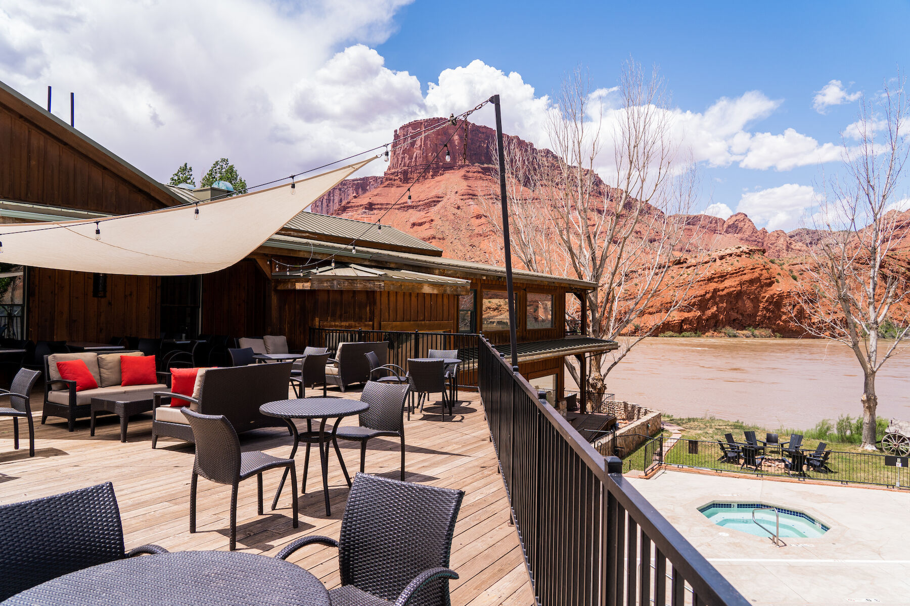 Outdoor seating area with tables and chairs, overlooking a river and red rock formations, clear sky above.