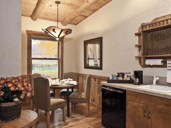 A cozy kitchen with wooden floors and ceilings, a small dining table, chairs, cabinets, and a window allowing natural light in.