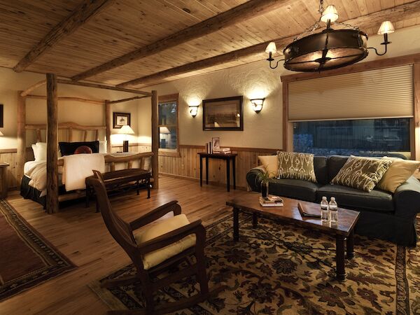 A cozy rustic room features a bed, sofa, coffee table, chairs, warm lighting, and wooden decor elements for a comfortable and inviting ambiance.