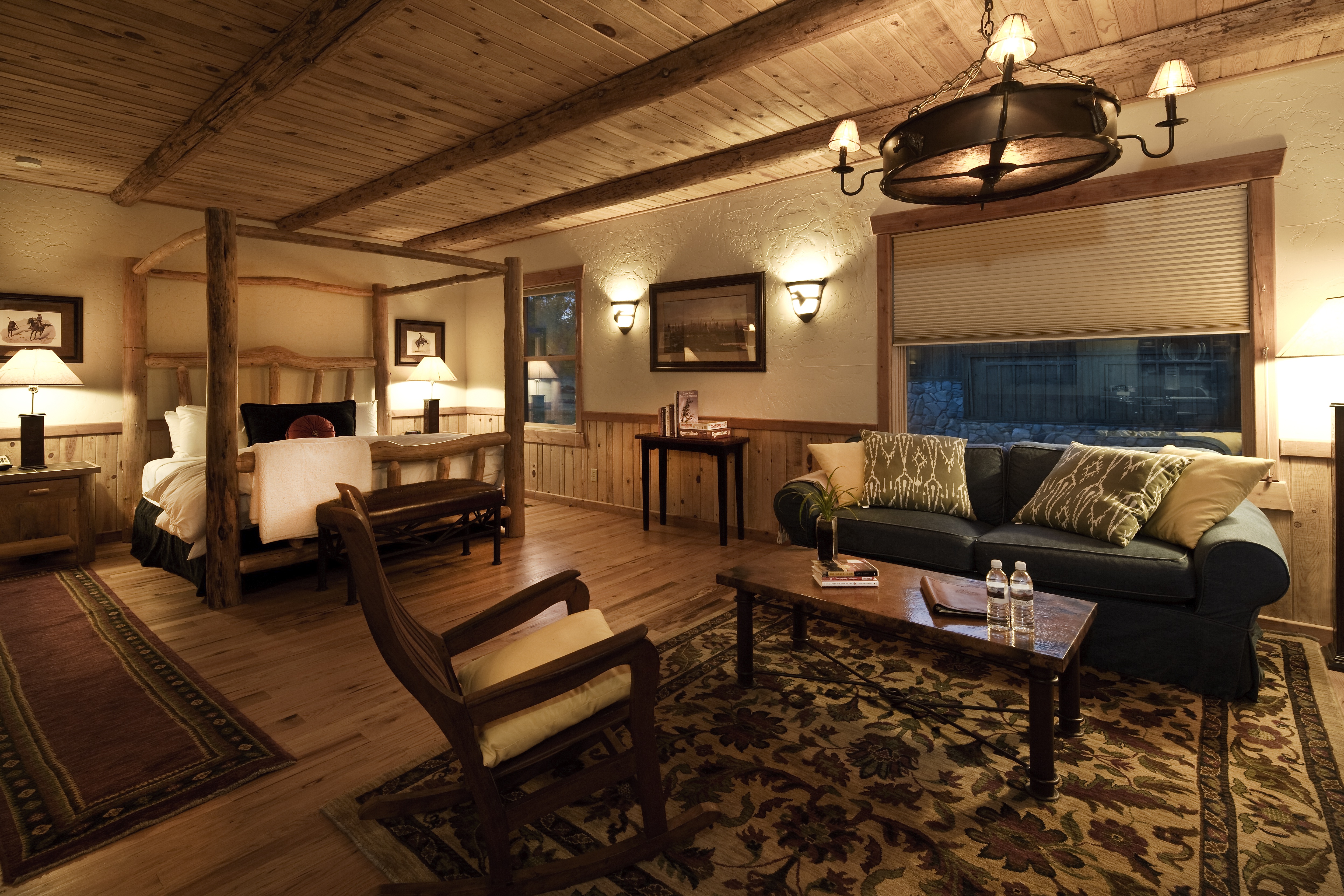 A wide view of a luxurious room with a four-poster bed, sofa, coffee table, and chandelier.