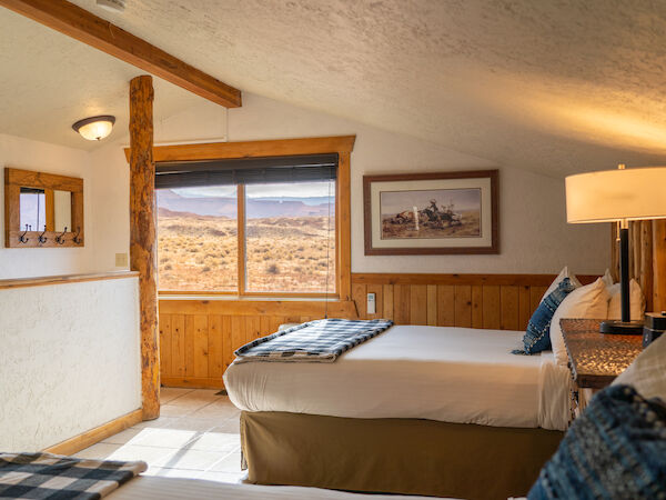 A cozy room with two beds, rustic decor, and a window view of a desert landscape.