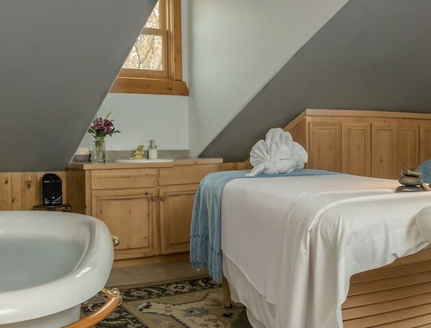 This image shows a tranquil spa room with two massage tables, a bathtub, and relaxing decor.