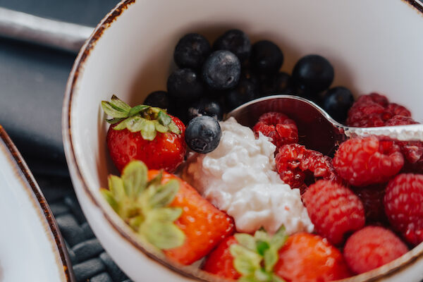 A bowl with strawberries, blueberries, raspberries, and cottage cheese, with a spoon inside.