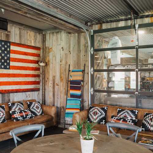 A cozy room with leather sofas, American flag wall art, and a glass garage door, featuring rustic decor and patterned cushions.