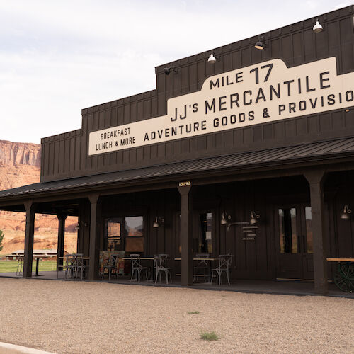 A rustic building labeled "JJ's Mercantile" offering adventure goods, with a desert landscape in the background.