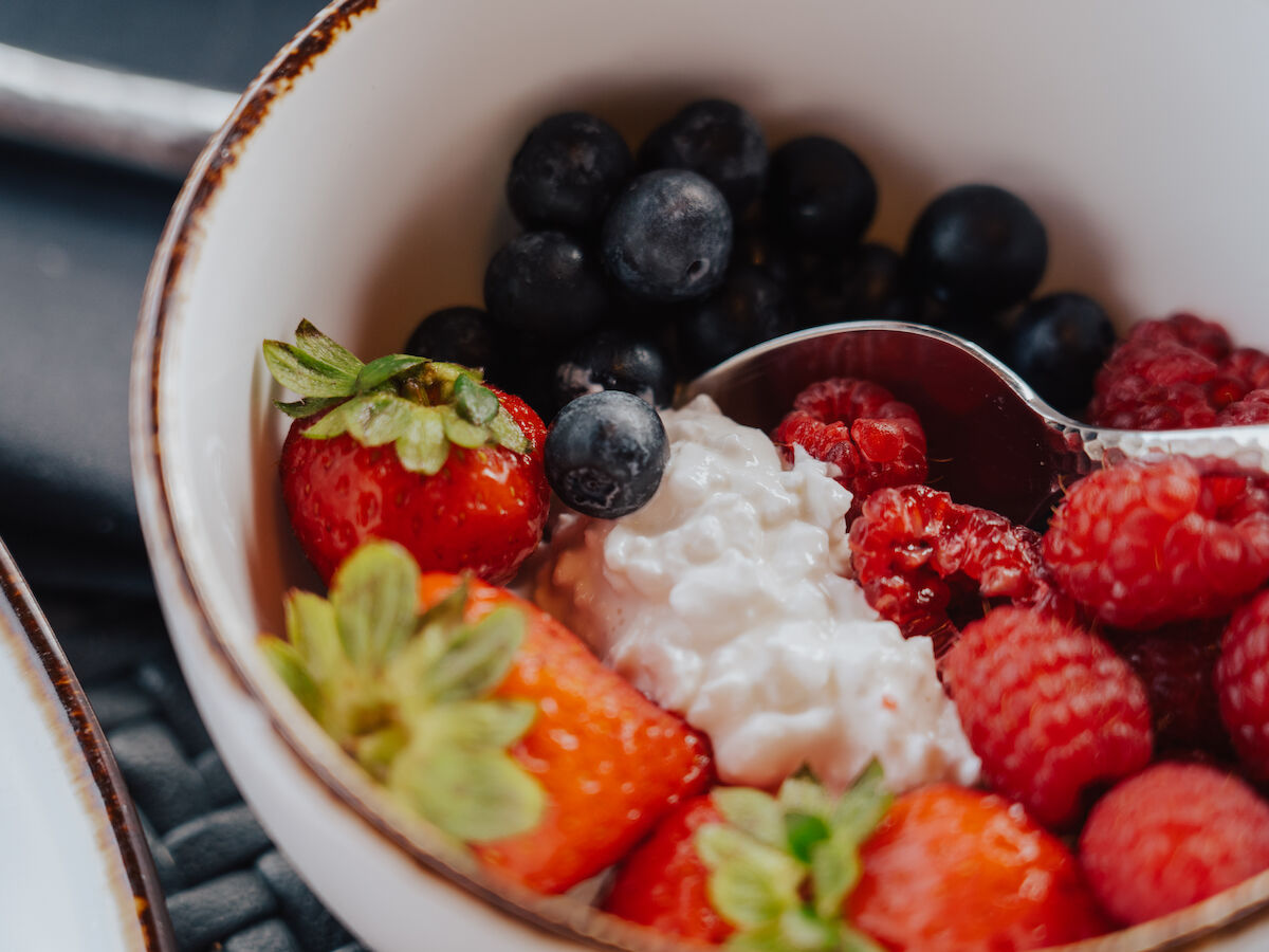 A bowl with strawberries, blueberries, raspberries, and cottage cheese, with a spoon inside.