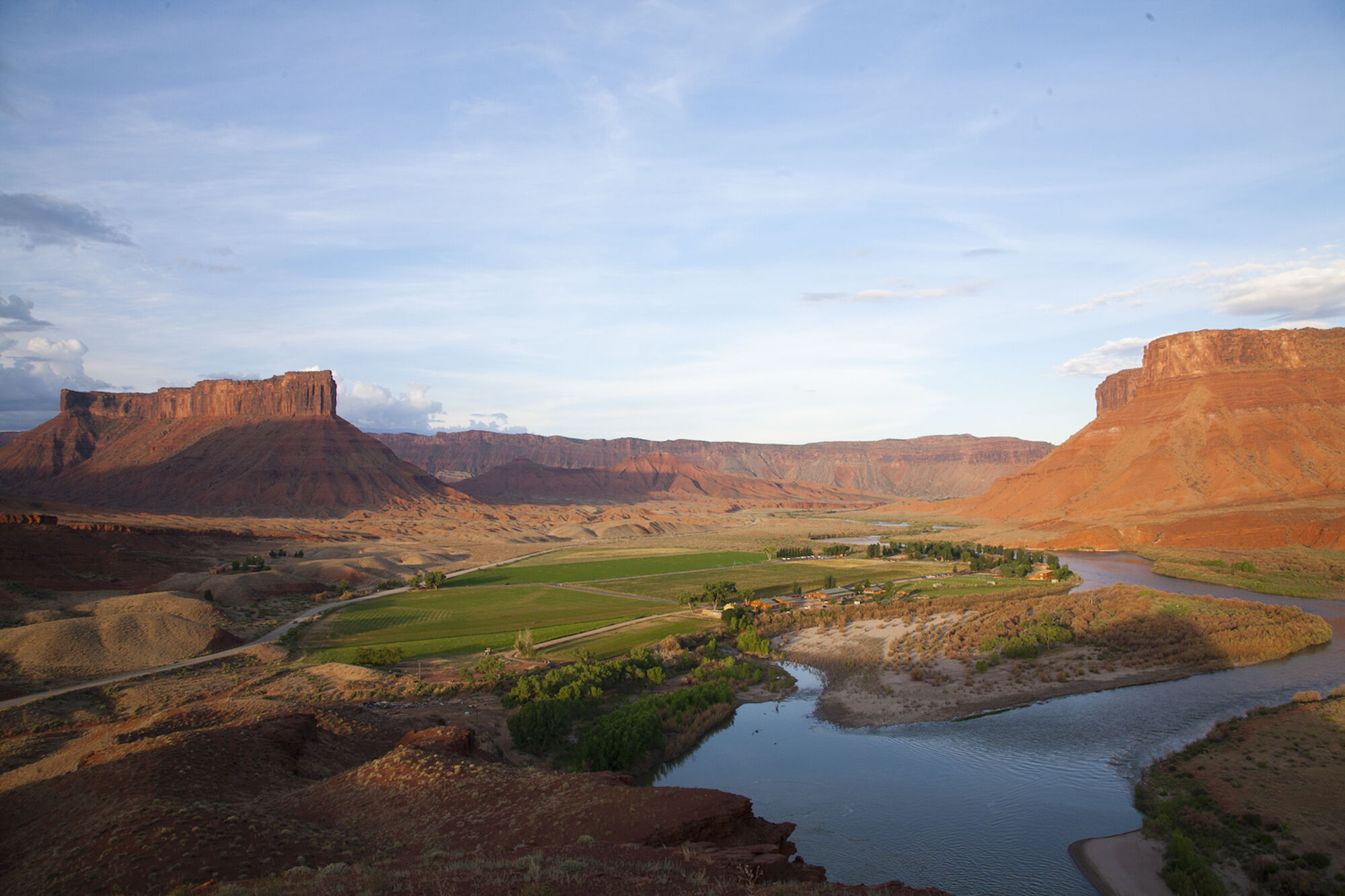 A scenic landscape with a river, greenery, and large red rock formations under a blue sky, creating a picturesque view.