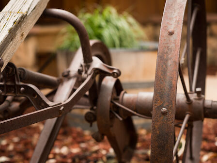 Close-up of a rusty vintage wagon wheel and metal parts, with blurred greenery in the background, creating a nostalgic atmosphere.