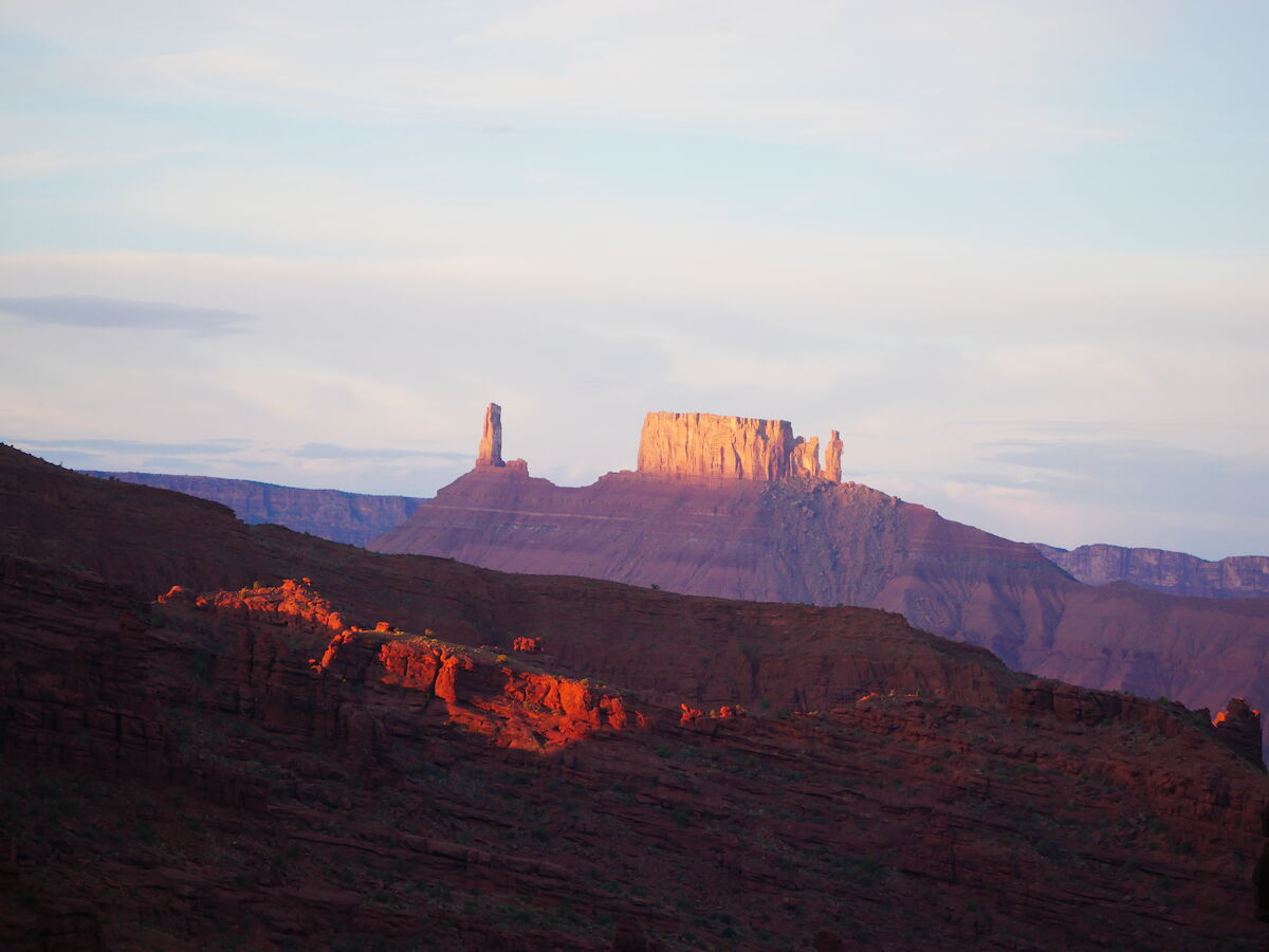 A scenic view of a mesa and surrounding rock formations, bathed in warm sunset light, under a partly cloudy sky.