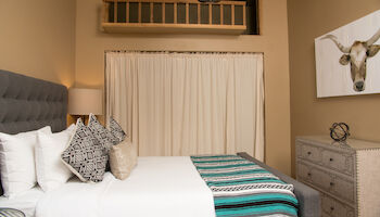 A cozy bedroom with a bed, decorative pillows, a lamp, a dresser, and a wall art of a cow's head.