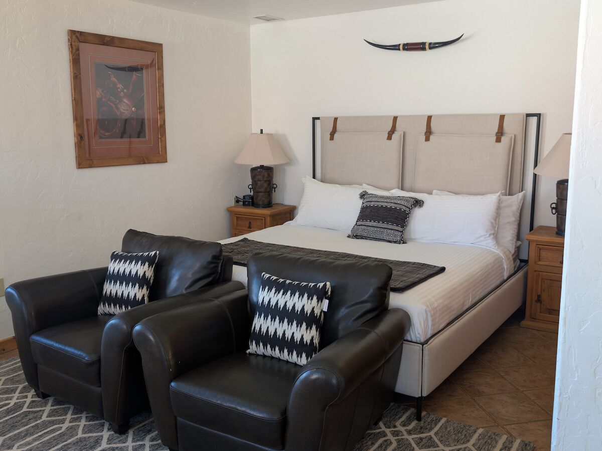 A cozy bedroom with a bed, two armchairs, patterned rug, wall decor, and lamps on wooden nightstands completes the inviting setup.