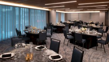 The image shows an elegant banquet hall with round tables set for a formal event, including black napkins, wine glasses, and floral centerpieces.