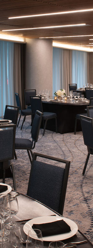 A banquet hall set up for an event with round tables, place settings, floral centerpieces, and dark chairs.