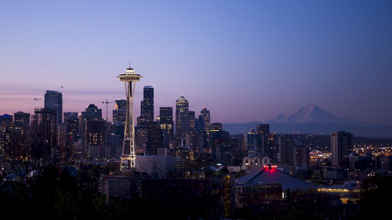 The image showcases the Seattle skyline at dusk, with the Space Needle prominently in the foreground and Mount Rainier visible in the background.